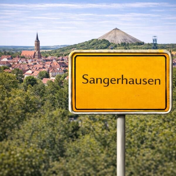 Gelbes Ortsschild Sangerhausen mit Stadt im Hintergrund